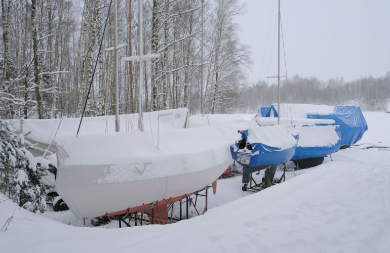 Zeilboten in winterstalling, afgedekt en bedekt met sneeuw