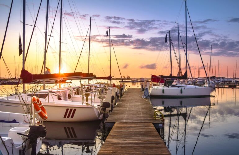Zeilboten aangemeerd aan houten stijger in een haven bij zonsondergang